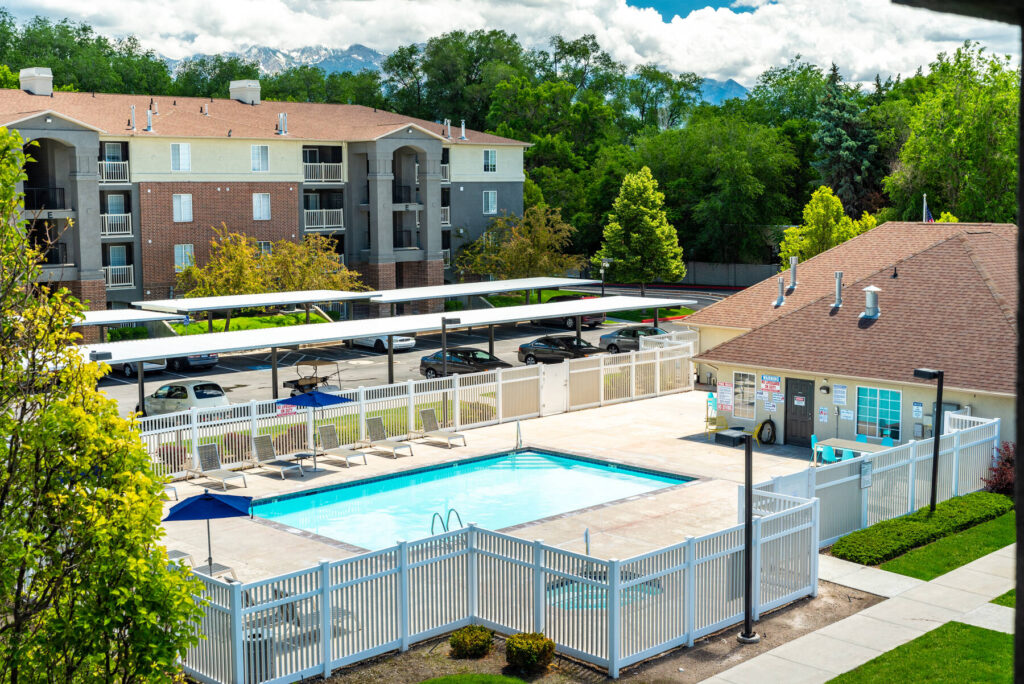 fenced pool with deck chairs, in the background is covered parking